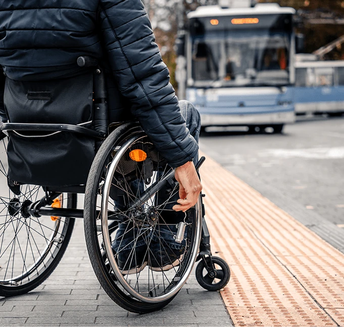 Oseba v invalidskem vozičku, ki čaka na avtobus pri taktilnih oznakah